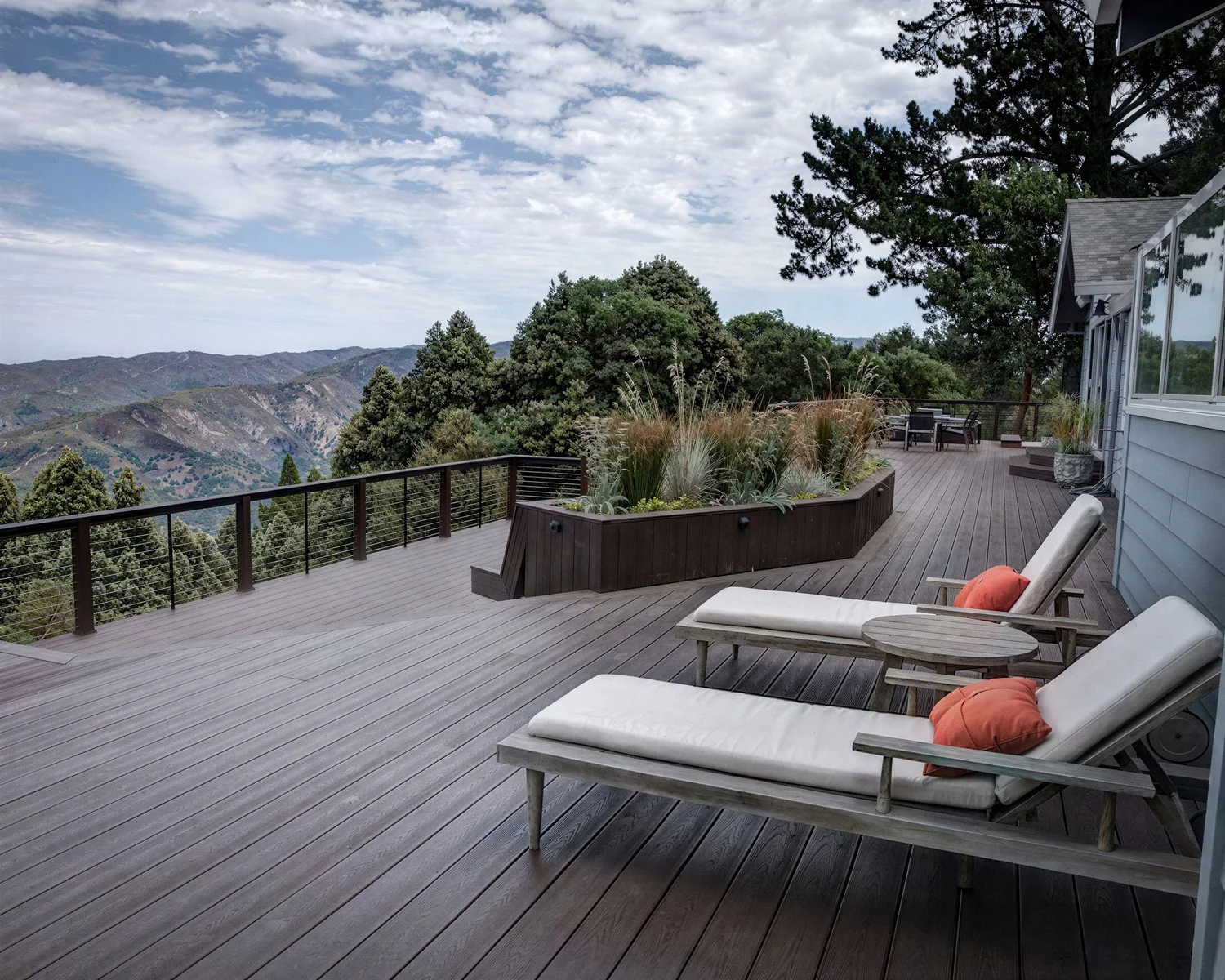 A wooden deck with lounge chairs overlooking a forested mountain valley.